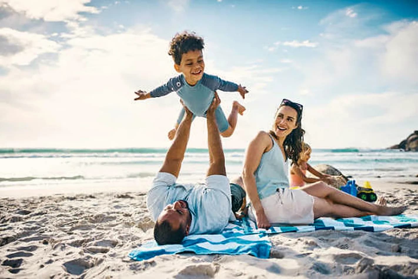 A father lifting his son into the air on the beach while mum laughs